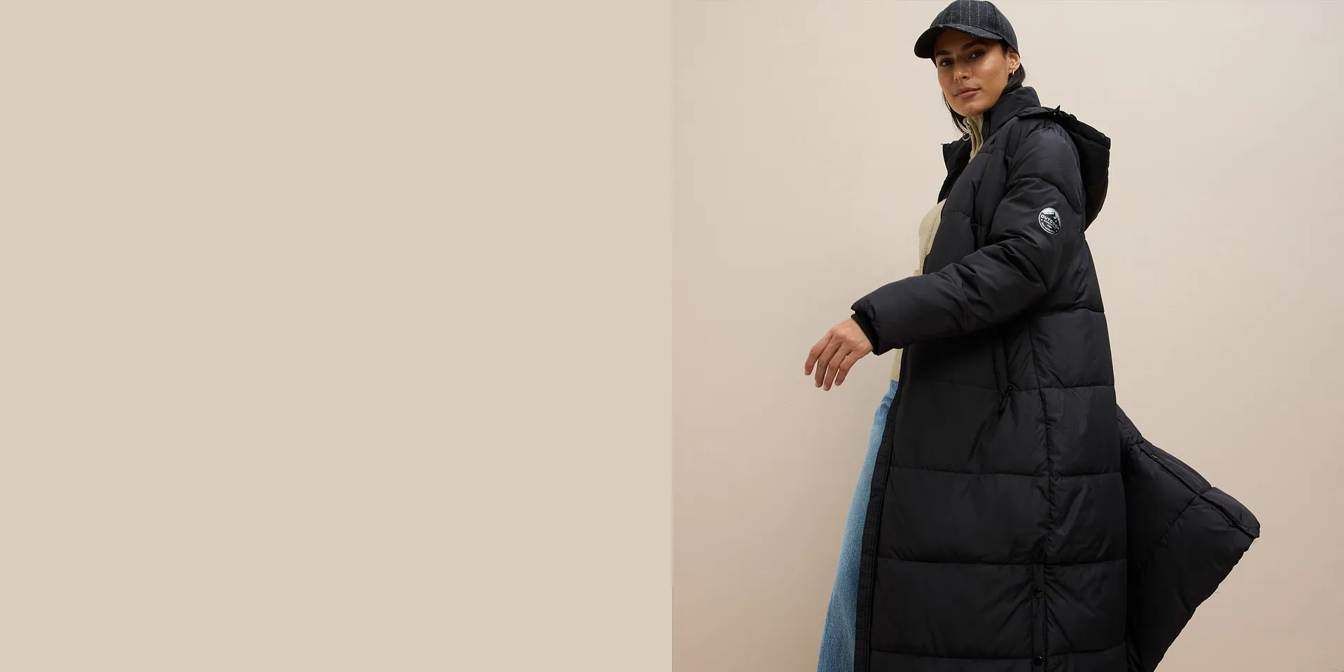 Lang, sort dunkåpe over beige genser, vide jeans og lue fullfører looken.