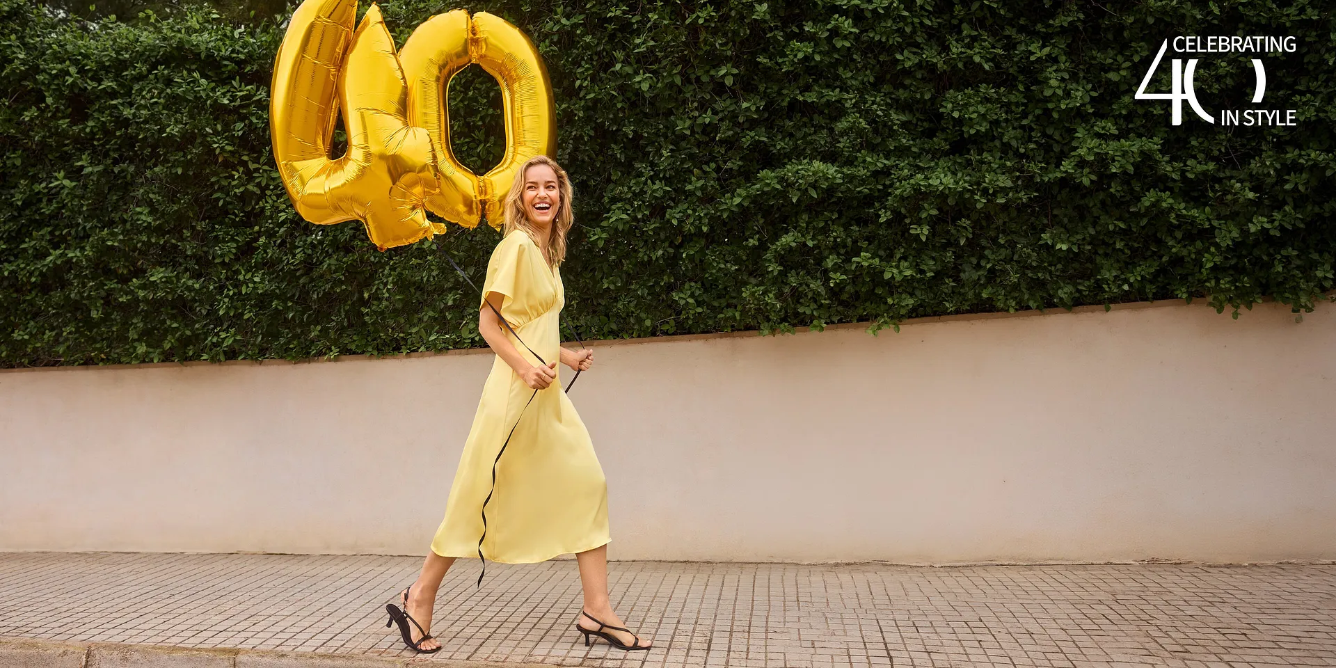 En gul sommerkjole med korte ermer kombinert med elegante, sorte sandaler.