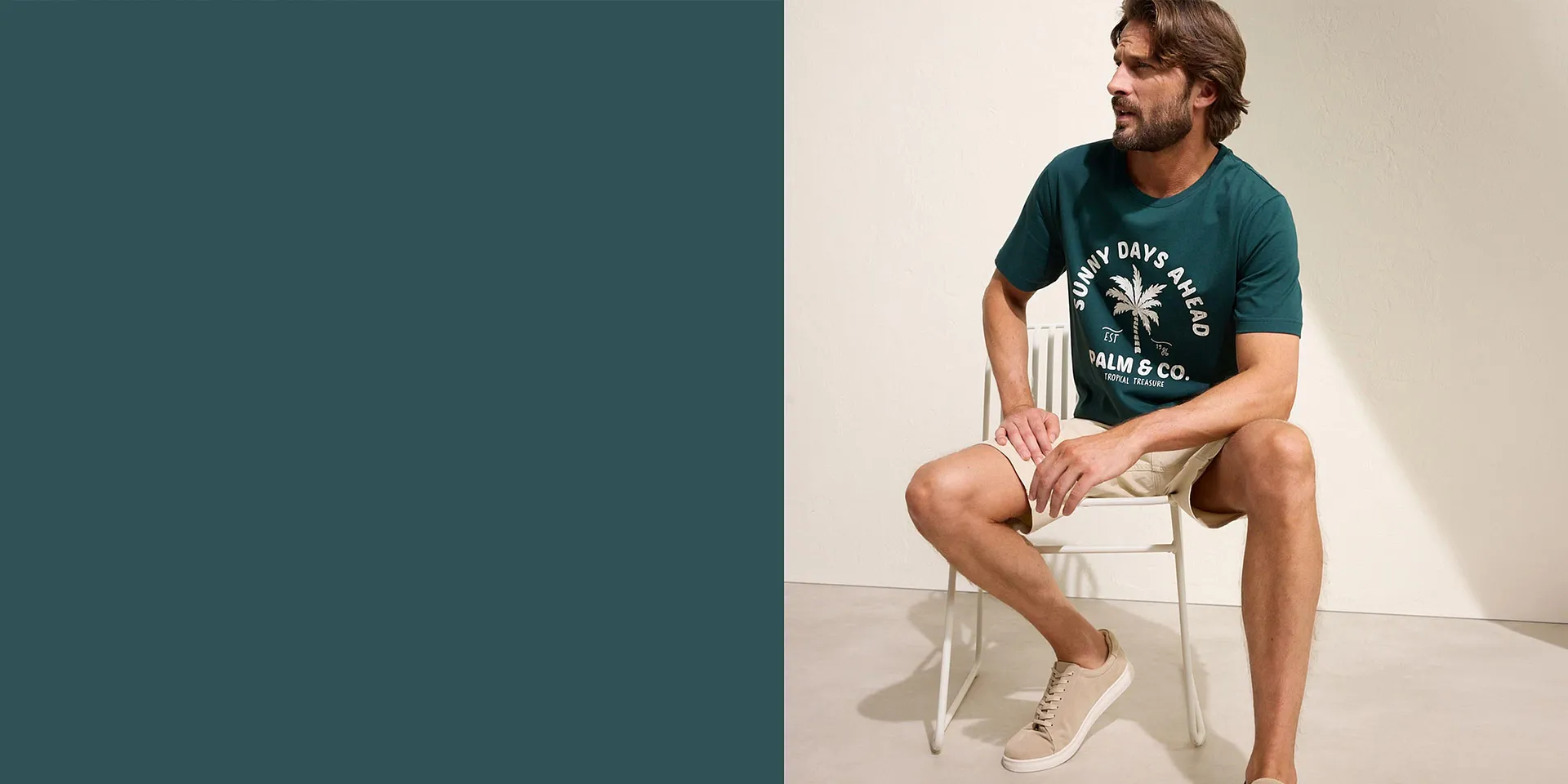 Mann i grønn T-skjorte med palmetrykk, beige shorts og hvite sneakers.