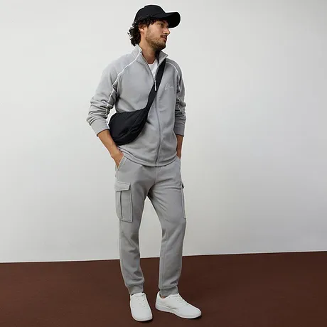 Avslappet, grå treningsdress med glidelåsjakke og hvite sneakers.