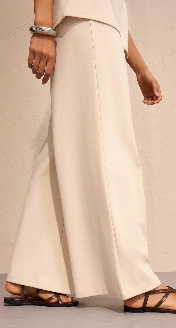 Elegant, kremhvit bukse med vide ben kombinert med flate sandaler.