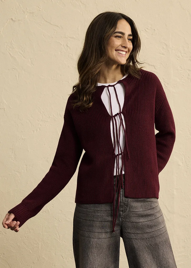 Kombo bestående av vinrød cardigan, hvit bluse med knytebånd og grå bukse.