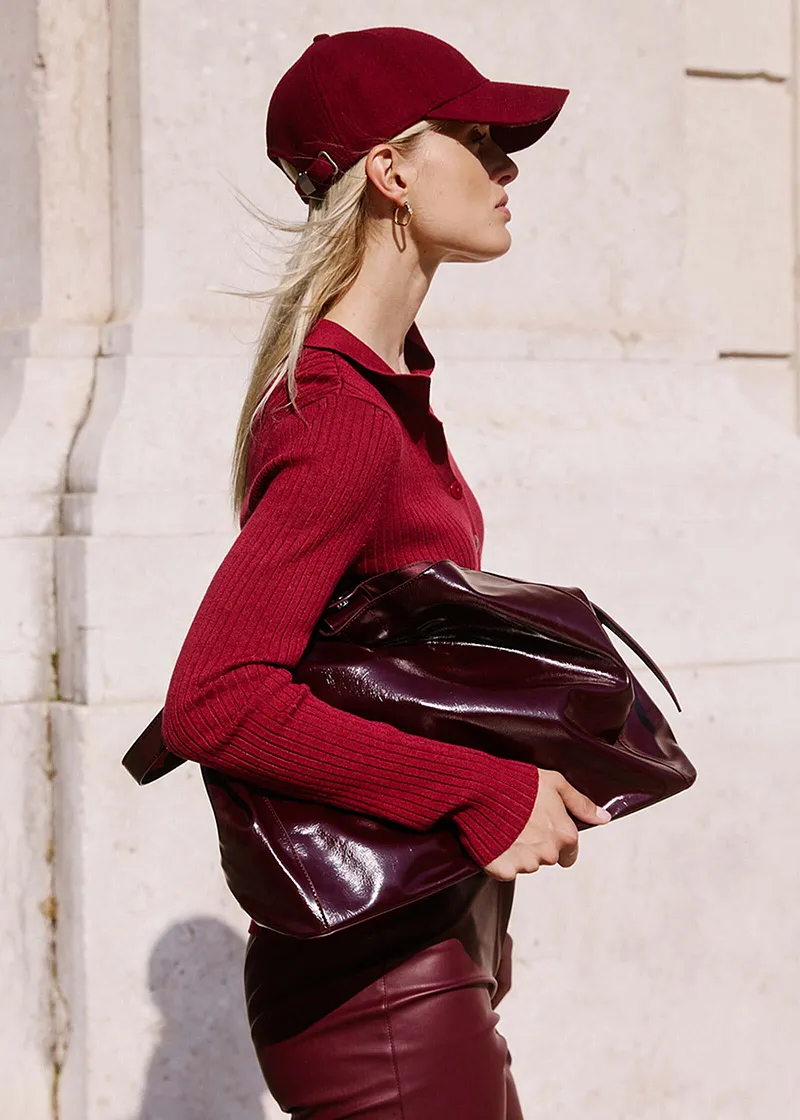 Elegant, burgunderrød look: Strikket genser, skinnbukse, baseball caps og glinsende veske.