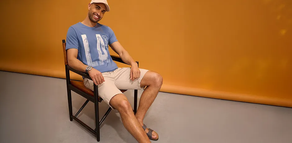 Blå T-skjorte med trykk, lyse shorts, baseballcaps og sandaler.