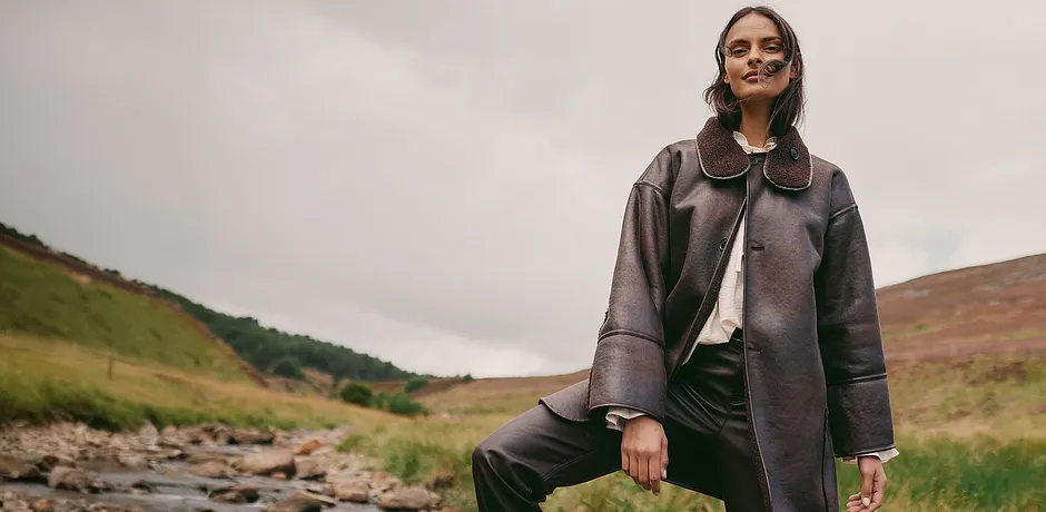 Elegant, brun skinnkåpe med stor krage kombinert med en lys topp og mørk bukse.