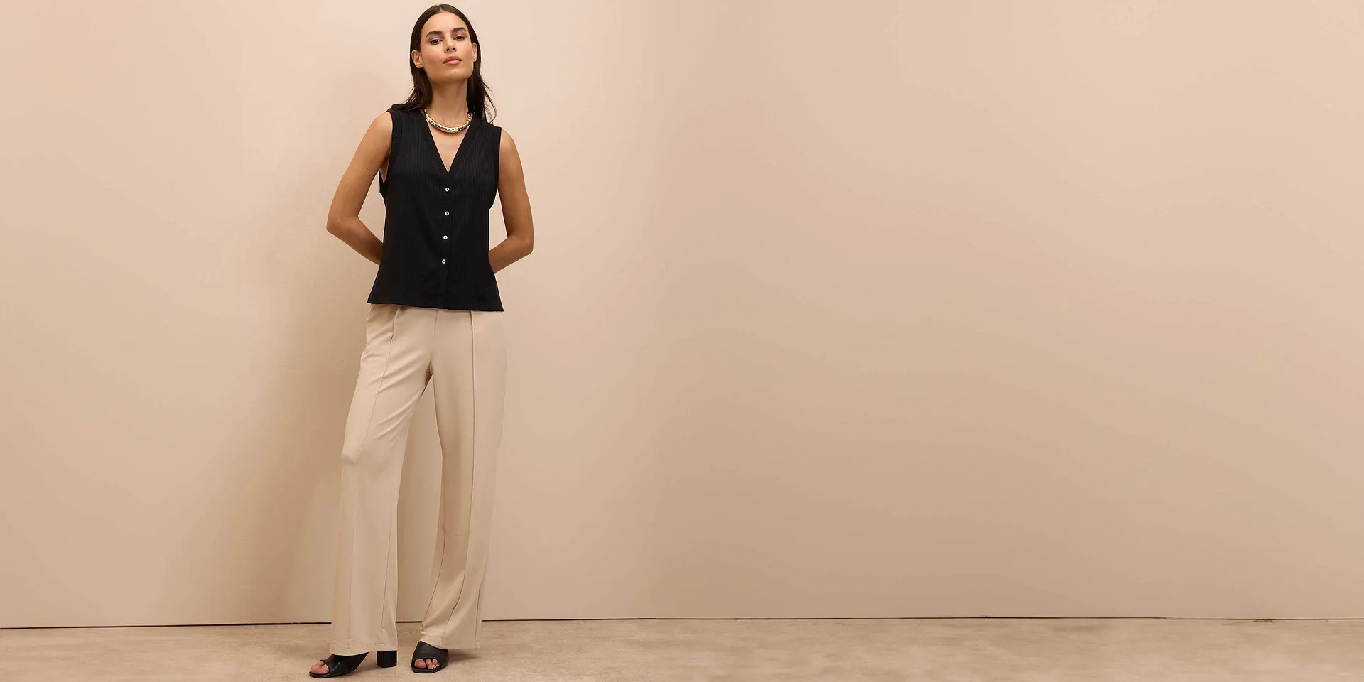 Elegant, sort vest med knapper kombinert med vid bukse i beige og sorte sko.