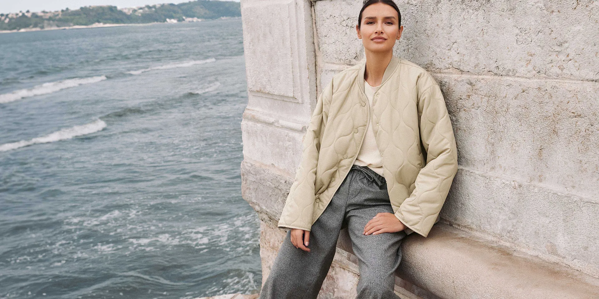 Ledig høstlook: Beige jakke, lyseblå jeans og hvit topp ved sjøen.