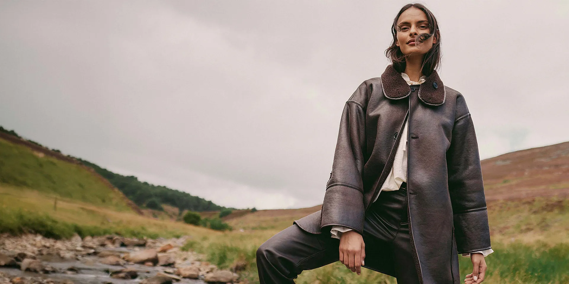 Elegant, brun skinnkåpe med stor krage kombinert med en lys topp og mørk bukse.