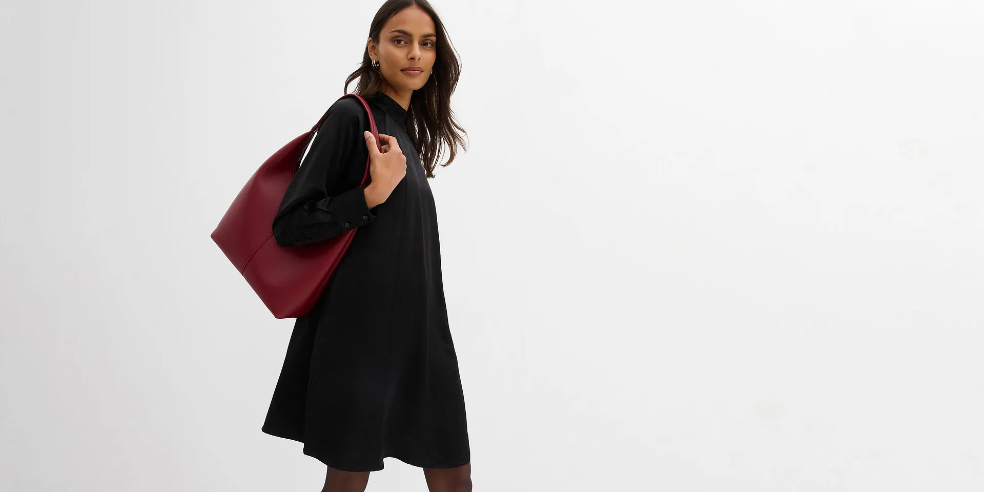 Sort kjole med h&oslash;y krage og hvit pynt p&aring; kragen. Kort modell med lange ermer.