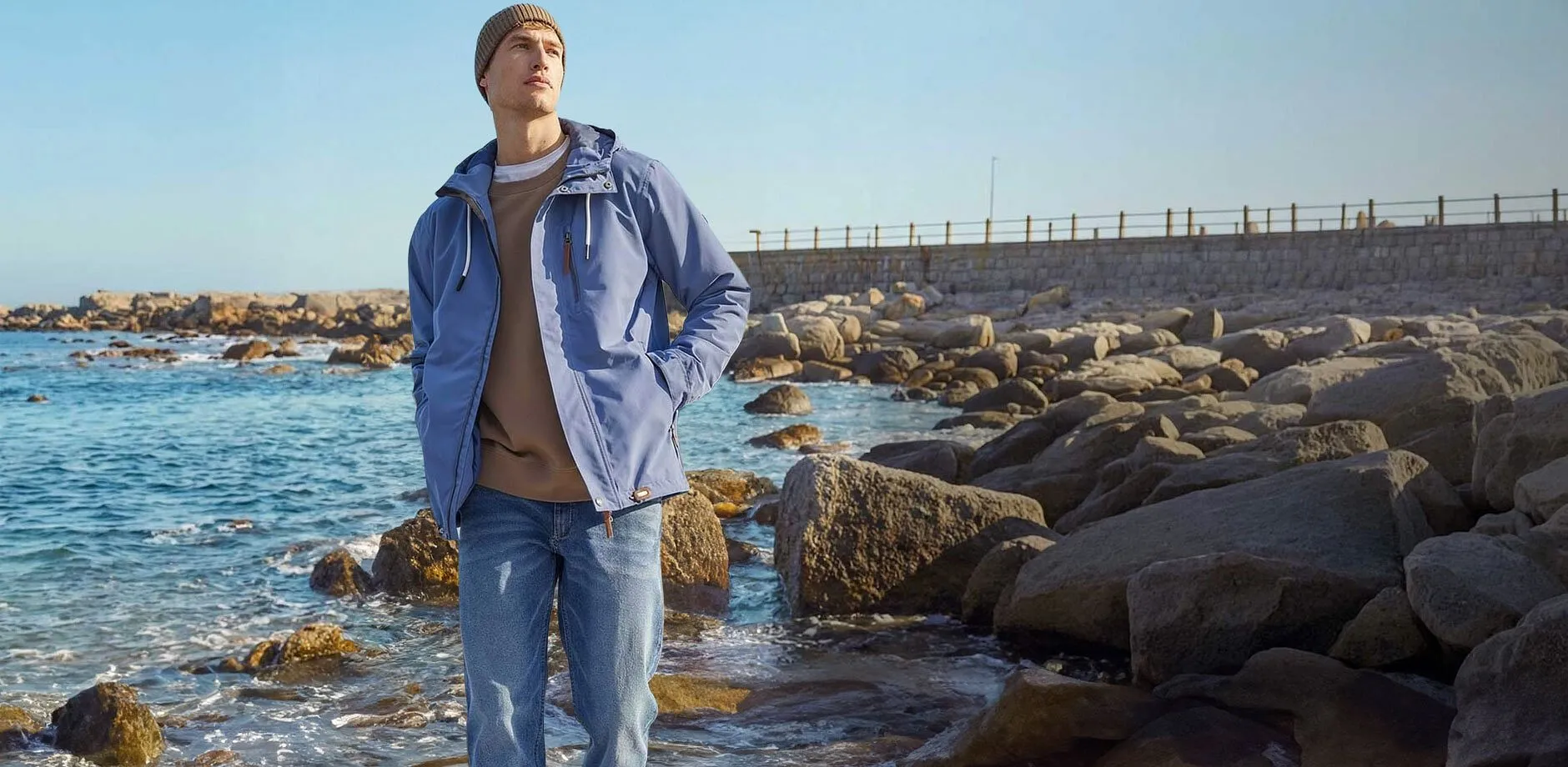 Stilig, bl&aring; funksjonsjakke og lyse jeans p&aring; stranden.