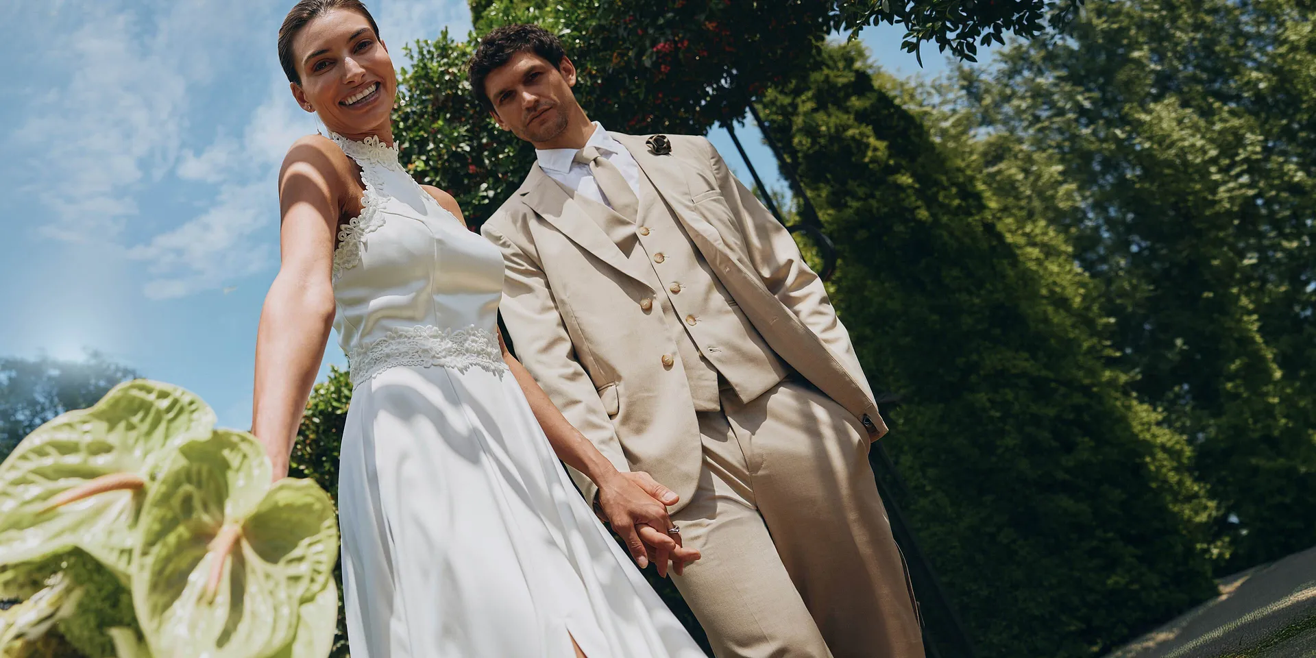Flott brudepar i solskinn: Hun i hvit kjole, han i beige dress.