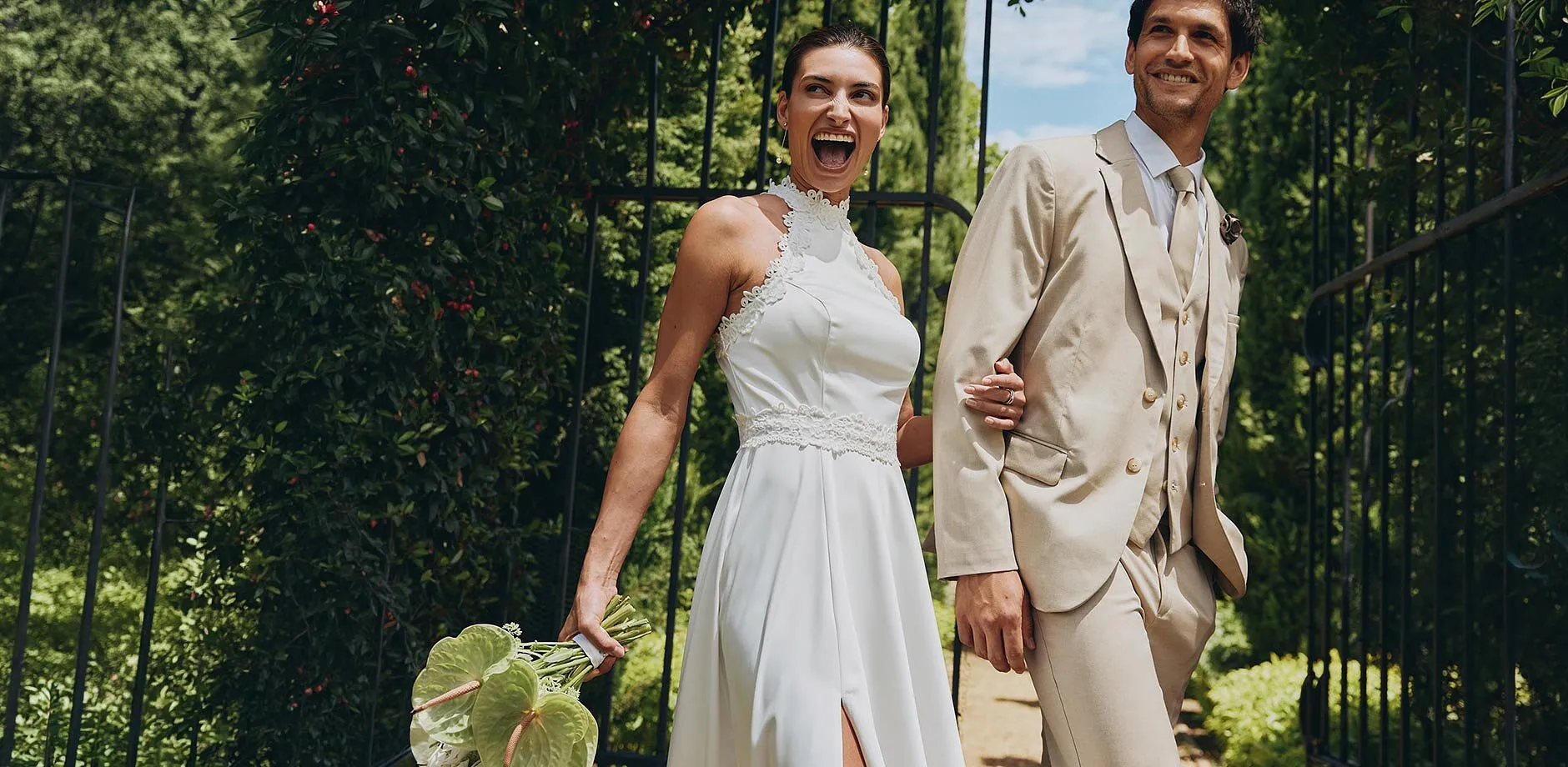 Flott brudepar i solskinn: Hun i hvit kjole, han i beige dress.