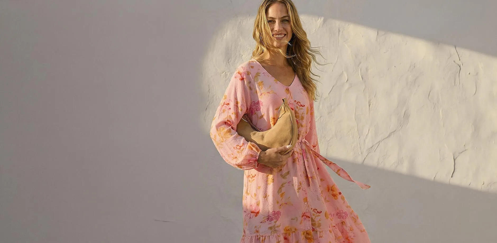 Kvinne i luftig rosa sommerkjole med blomsterprint og lange ermer.