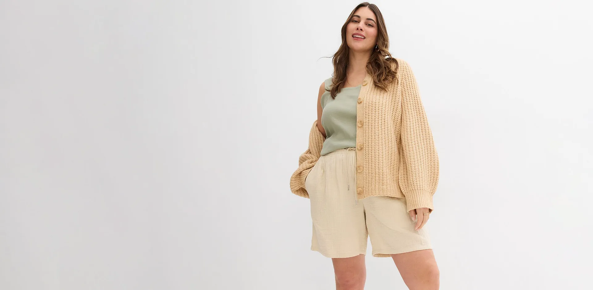 Kvinne i beige cardigan, lysegr&oslash;nn singlet og kremfarget shorts.