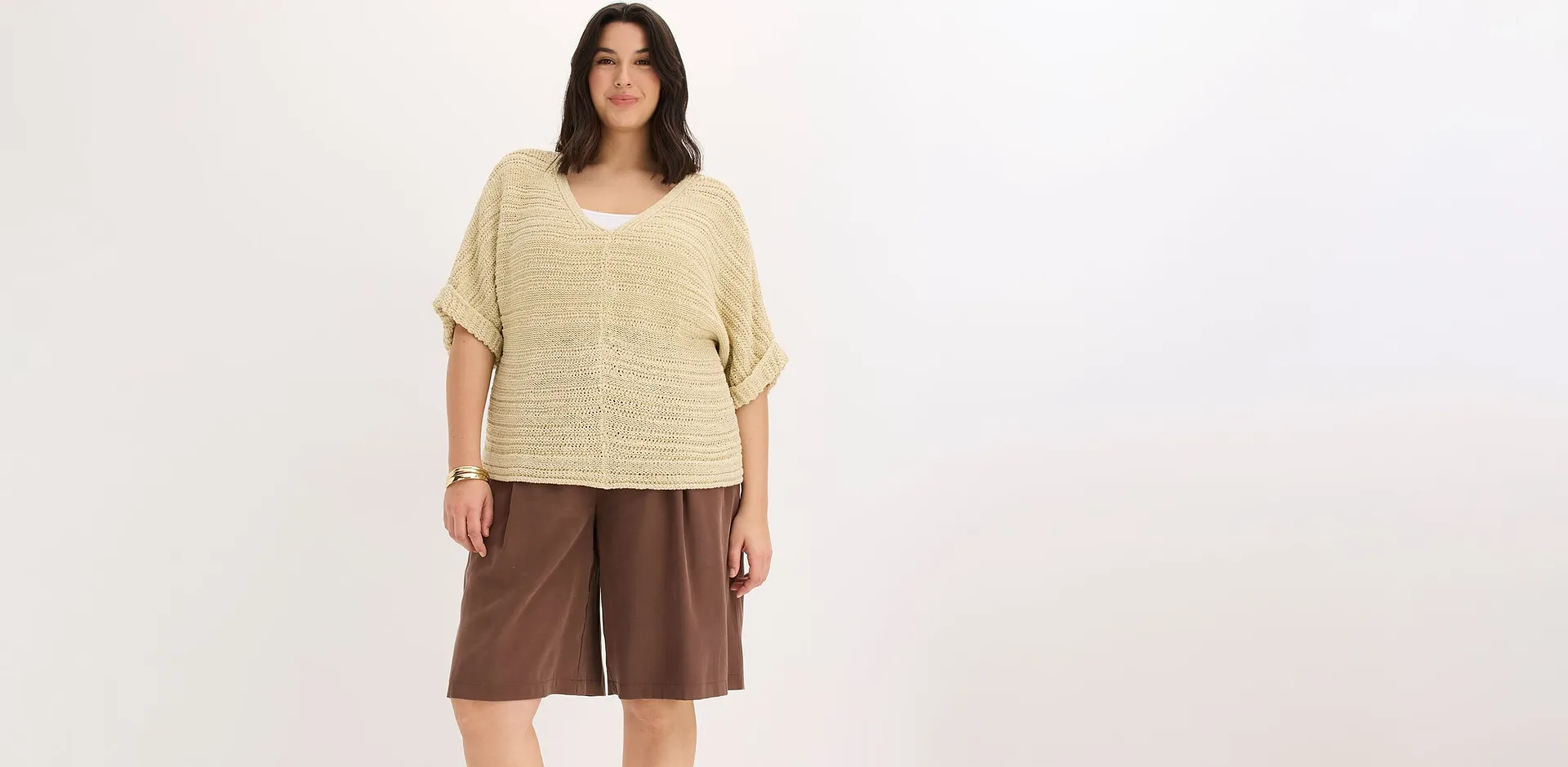 Person i beige, strikket topp og brun, vid shorts.