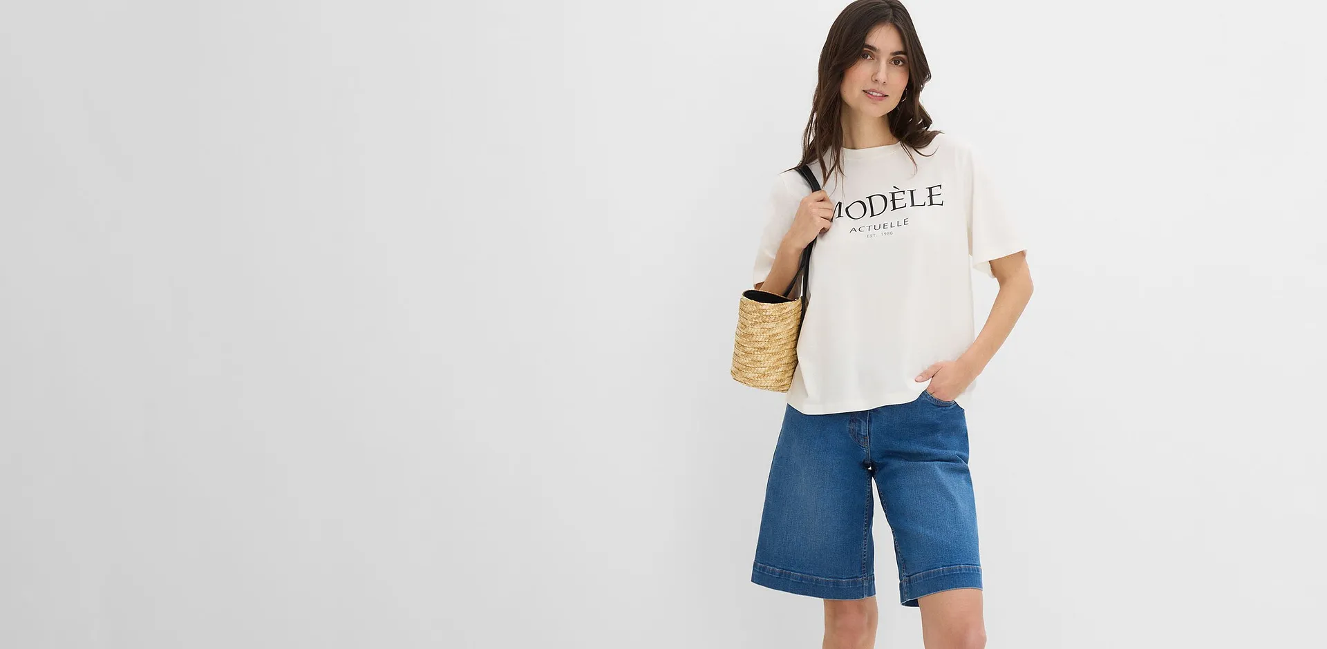 Person i avslappet, hvit T-skjorte med skrift og vid bermudashorts i denim.