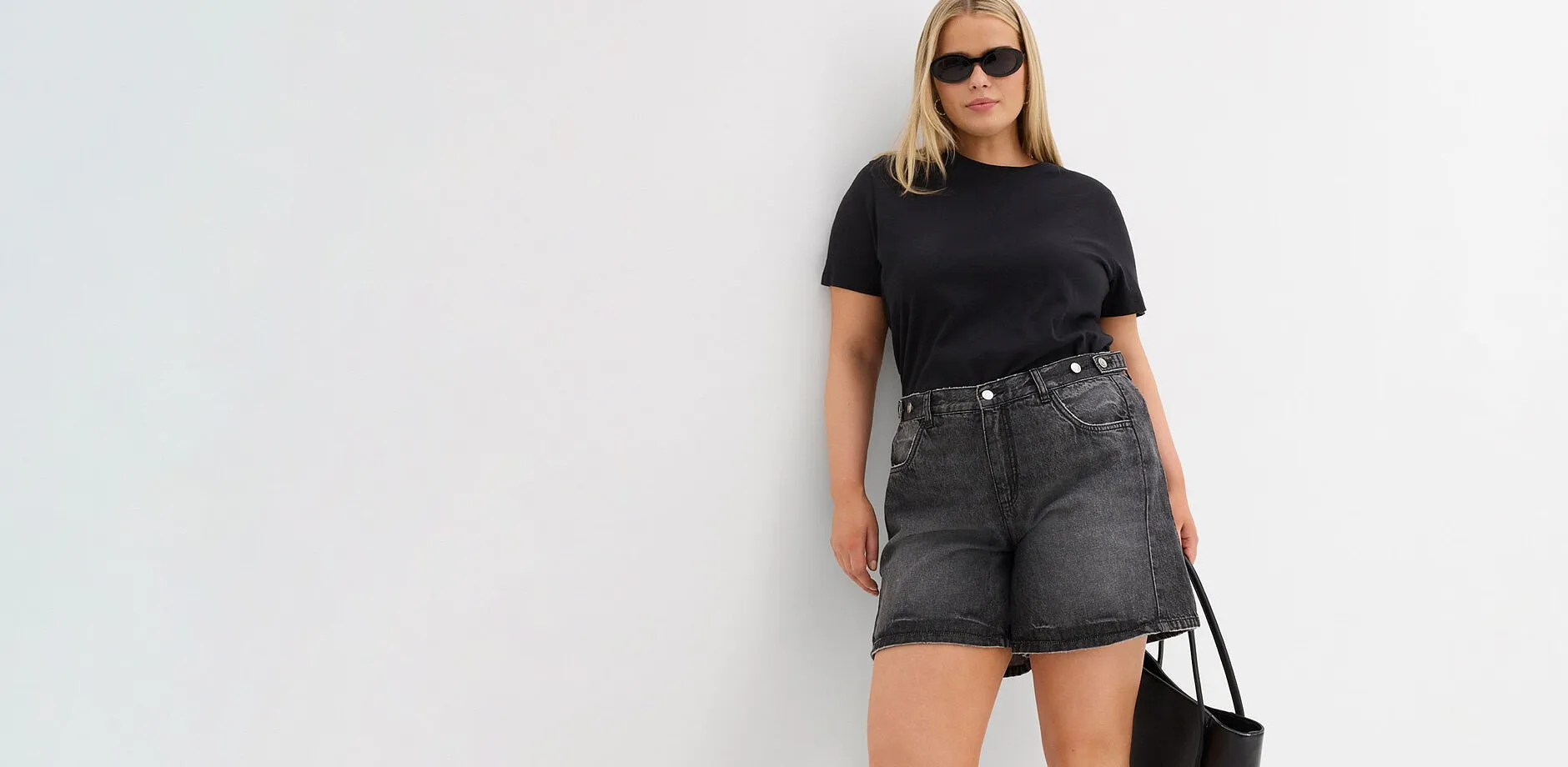 Sort T-skjorte, vid, gr&aring; denimshorts, solbriller og sort veske.