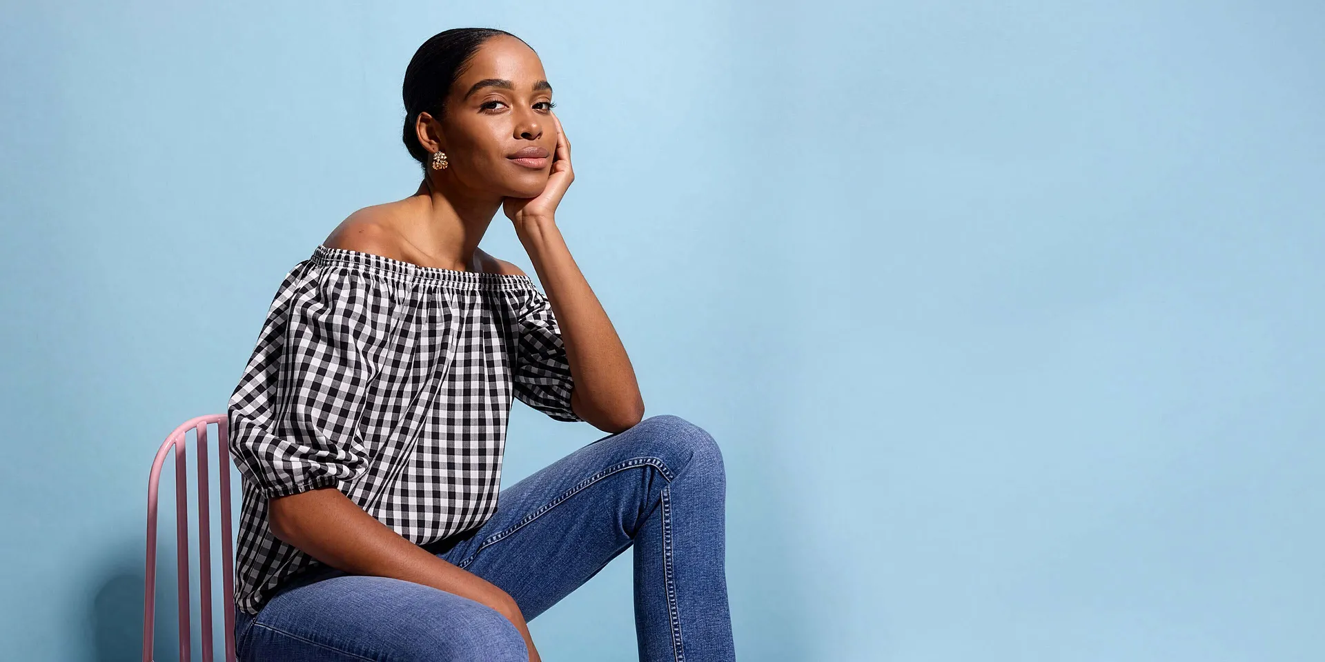 Person i sort- og hvitrutete off-shoulder-bluse og bluejeans.