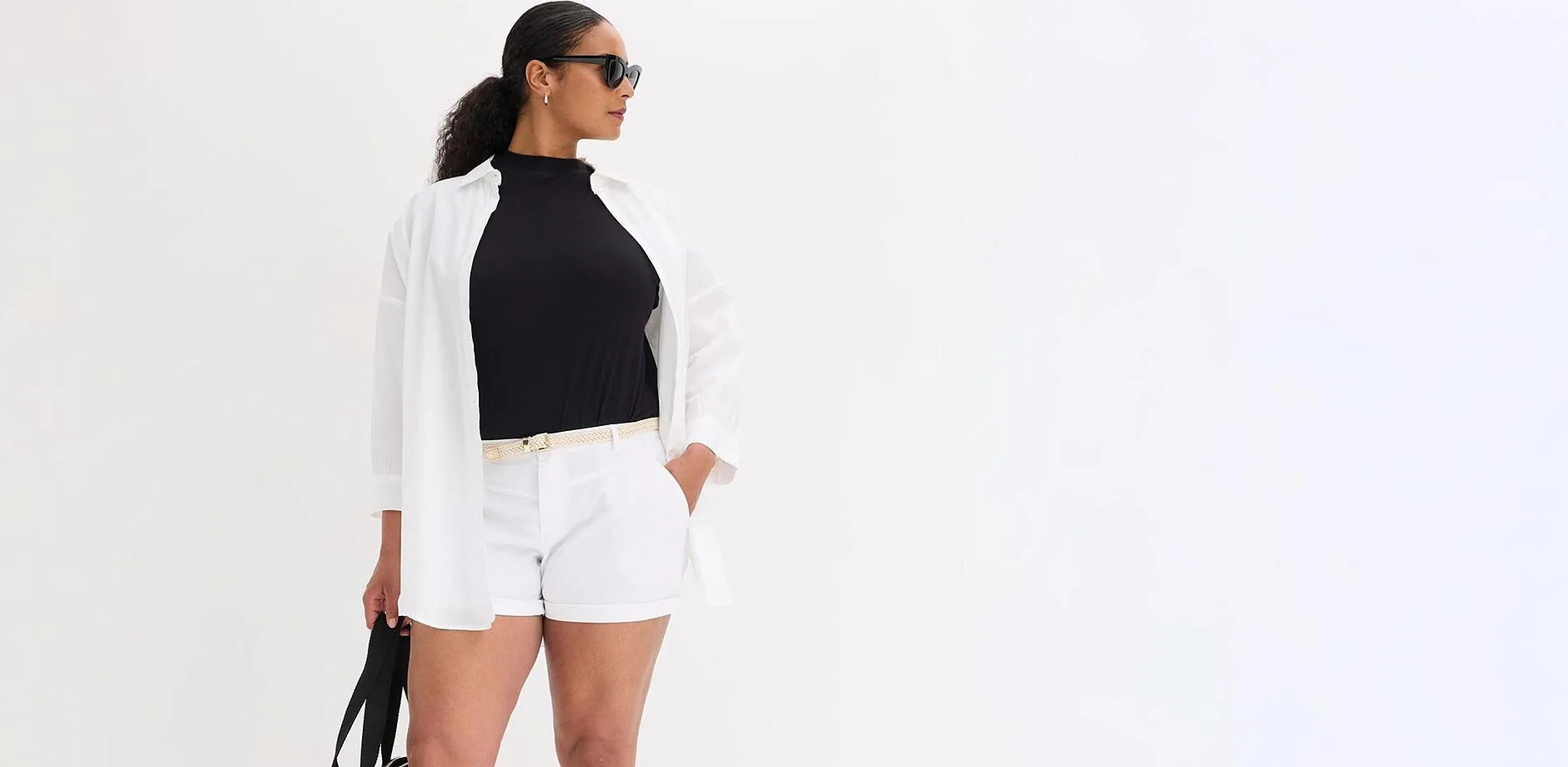 Hvit, &aring;pen skjorte over sort topp, hvit shorts, lyst belte og solbriller.