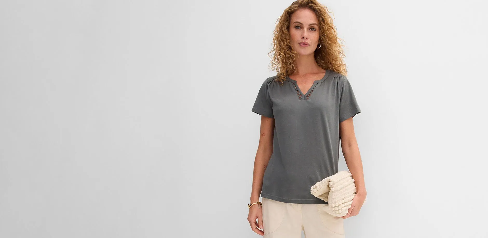 Gr&aring; T-skjorte med V-hals, lys bukse og beige veske i strukturert materiale.