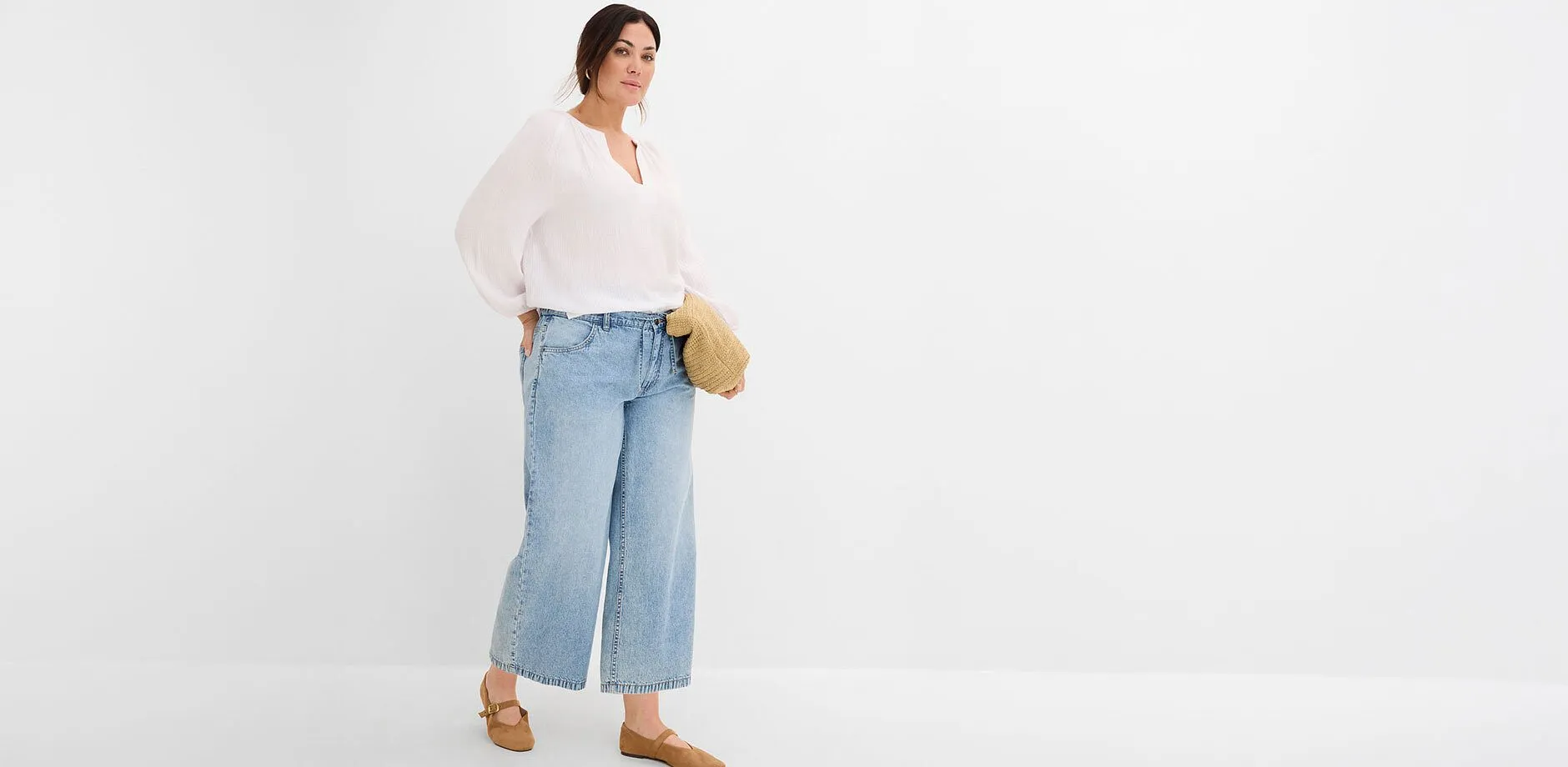 Vid, hvit bluse og vide jeans kombinert med brune sko og fletteveske.