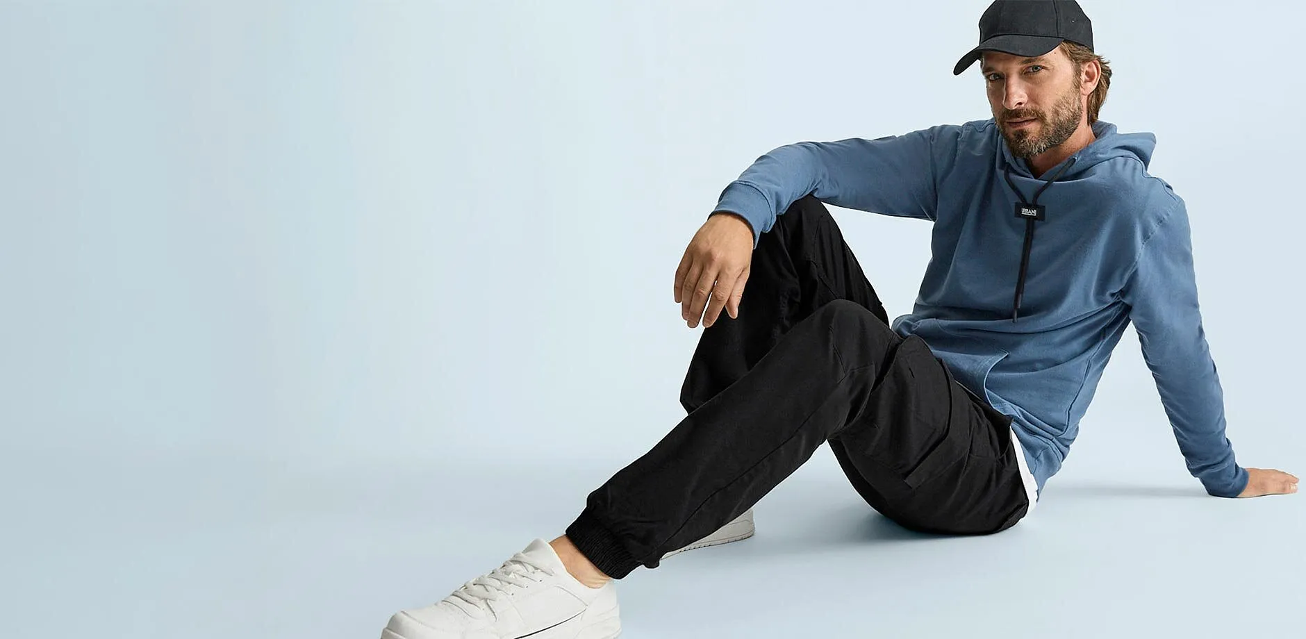 Bl&aring; hettegenser, sort cargobukse, hvite sneakers og sort caps skaper en avslappet stil.