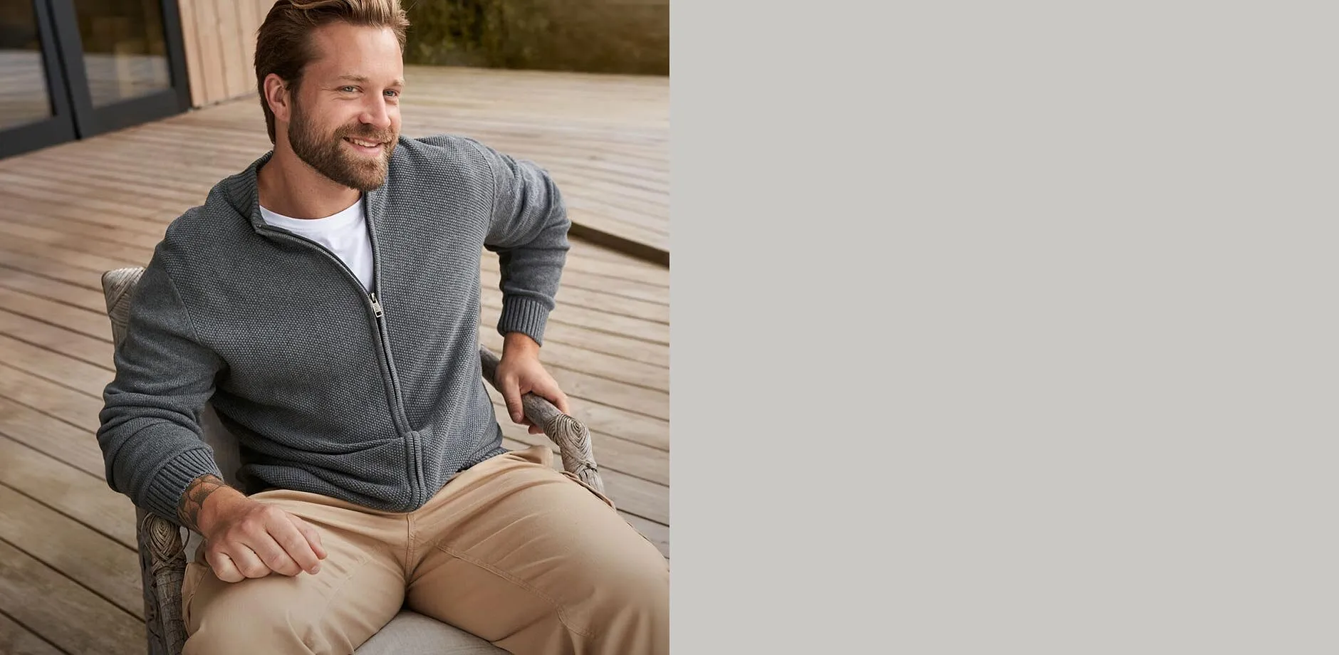 Hen i gr&aring; cardigan over hvit T-skjorte og beige bukse.