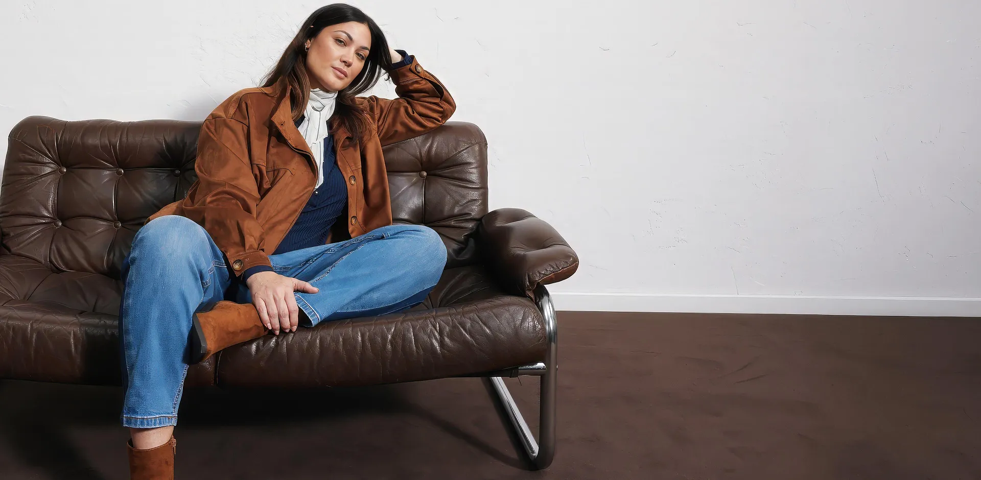 Jakke i imitert, semsket skinn, bluejeans, m&oslash;rk topp, lyst skjerf og st&oslash;vletter.
