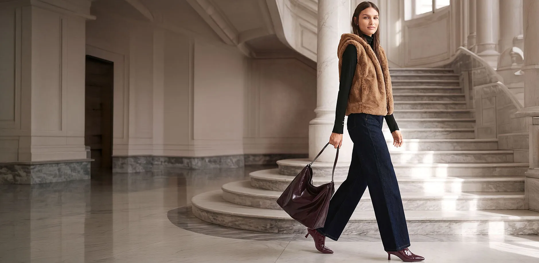 Brun fuskepelsvest, sort pologenser, vide jeans, burgunderfarget veske og ankelboots.