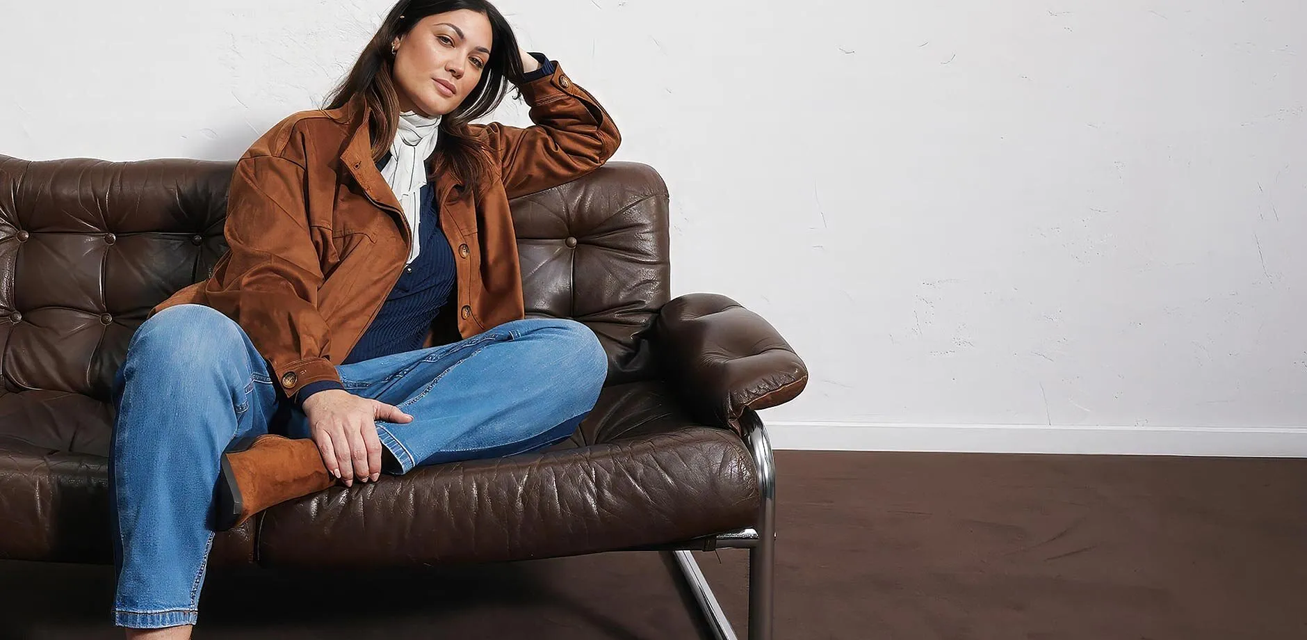 Jakke i imitert, semsket skinn, bluejeans, m&oslash;rk topp, lyst skjerf og st&oslash;vletter.