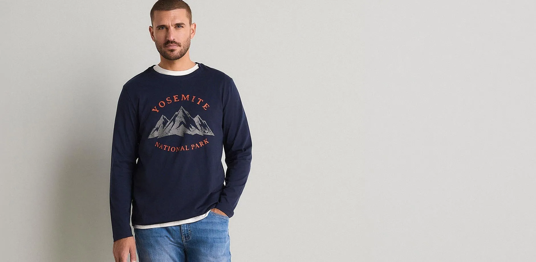 Hen i jeans og m&oslash;rkebl&aring; genser med Yosemite National Park-trykk.