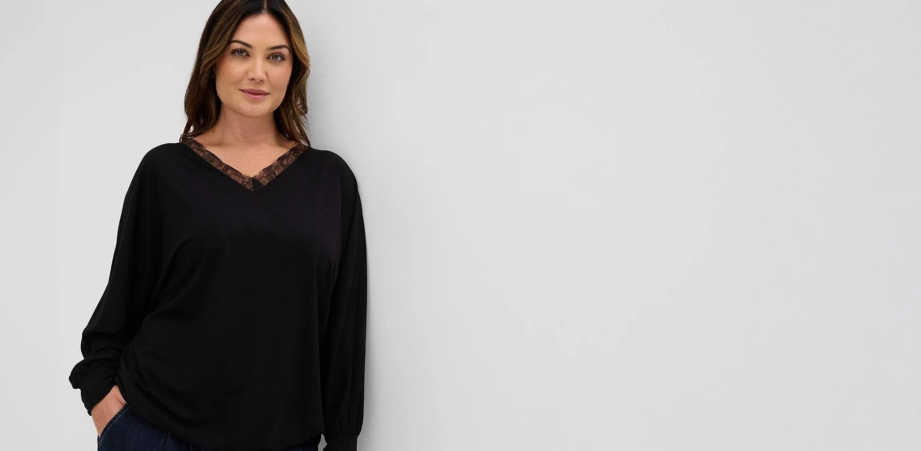 Moteriktig, sort og langermet topp med blonder i V-halsen og m&oslash;rke jeans.