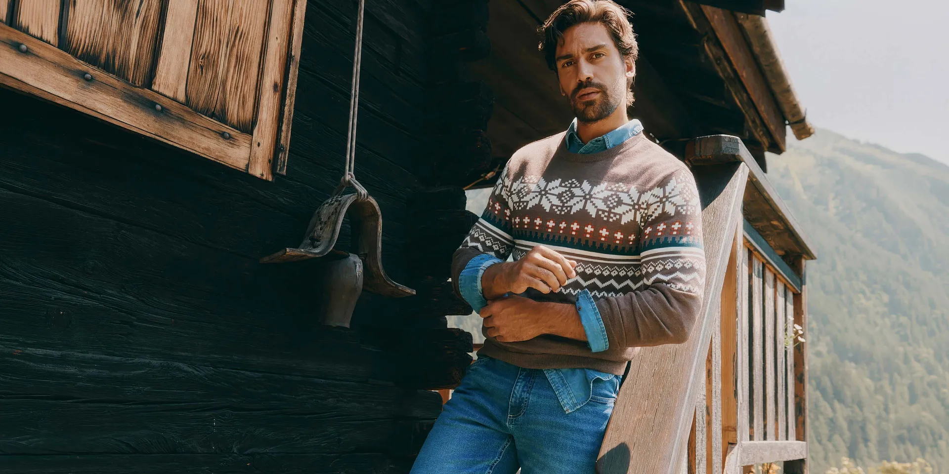 Hen i brun, m&oslash;nstret genser, denimskjorte og bl&aring; jeans.