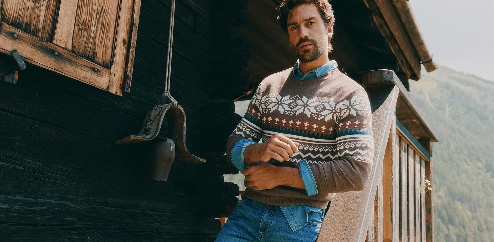 Hen i brun, m&oslash;nstret genser, denimskjorte og bl&aring; jeans.