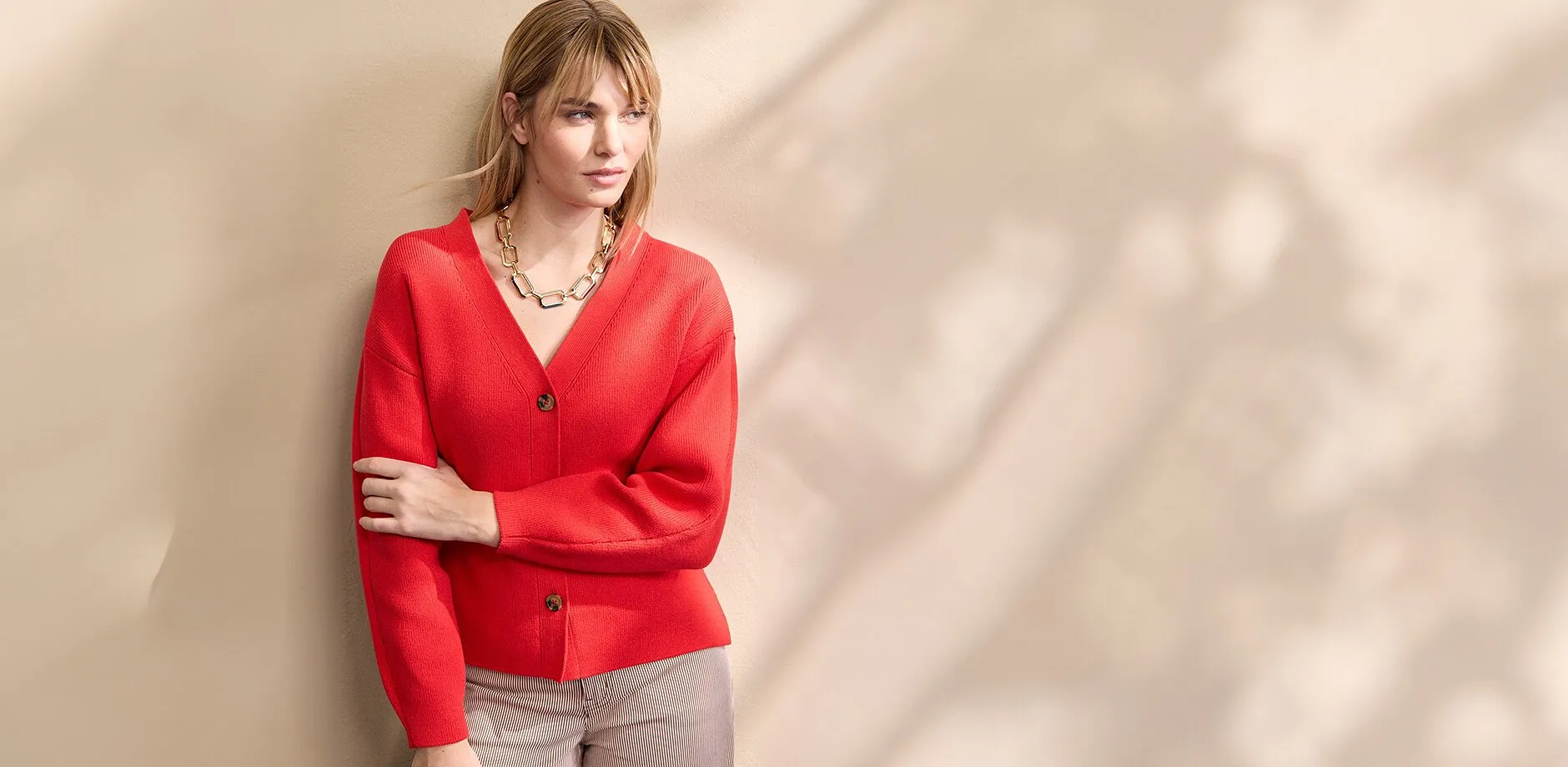 En knallr&oslash;d cardigan med V-hals og knapper kombinert med et i&oslash;ynefallende, gullfarget kjede.