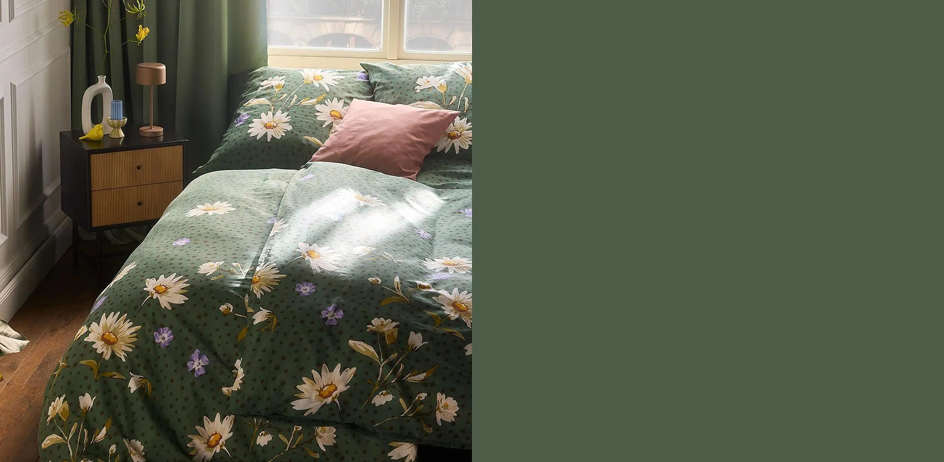 Gr&oslash;nt sengesett med blomsterm&oslash;nster pynter sengen sammen med matchende puter.