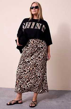 Kvinne med sort cropped-skjorte med SHINE-leo-trykk, matchende skjørt i leopardmønster, sorte solbriller og sort veske med glans