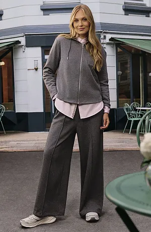 Grå hettegenser over en dus rosa bluse, kombinert med en vid grå bukse og hvite joggesko.