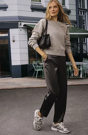 Casual streetstyle med beige genser, mørk bukse og hvite joggesko. Den sorte vesken setter prikken over i-en.