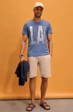 Blå T-skjorte med "LA"-trykk, lyse shorts, hvit caps og sandaler. Avslappet sommerlook.