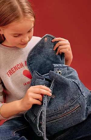 Grå sweatshirt med rød skrift og blå ryggsekk i denim. Ledig hverdagslook for unge mennesker.