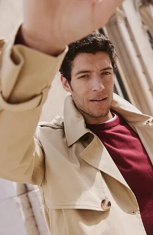 Elegant, beige trenchcoat over burgunderrød genser.