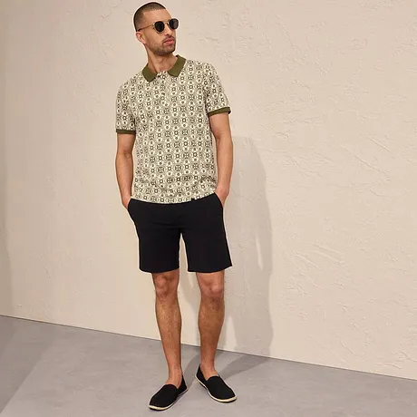Mønstret poloskjorte og mørk shorts for en ledig sommerlook, solbriller og espadriller kompletterer looken.