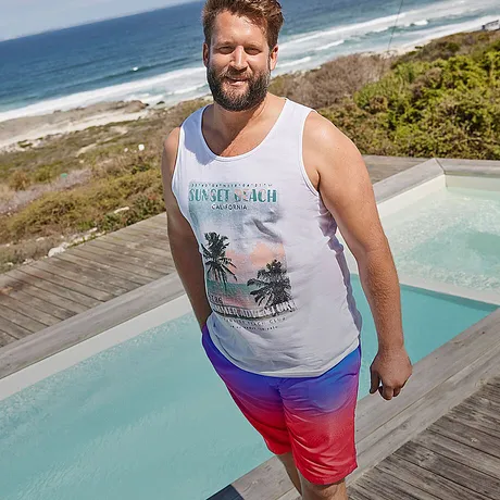 Hvit singlet med tropisk motiv, fargeglad rød og blå badeshorts.