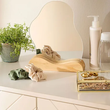 Beige hårbånd og hårstrikker på lys overflate ved siden av speil, planter og pleieprodukter.