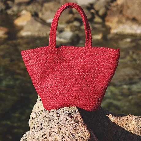 Lysende rød stråveske hviler på svaberget ved vannet, perfekt for sommerlige strandturer.