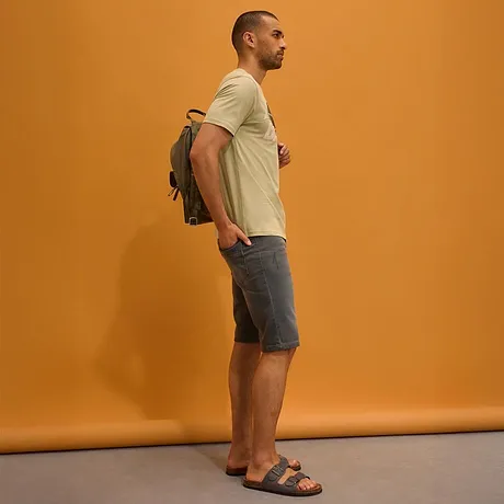 Lys T-skjorte, grå jeansshorts, sandaler og ryggsekk.