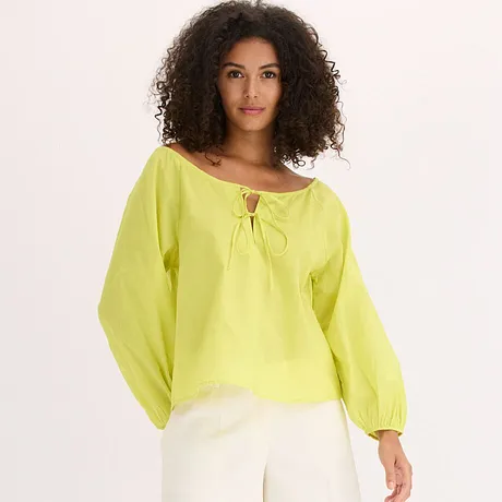 Luftig sitrongul bluse med vide ermer og knyting ved halsen, kombinert med hvite bukser.