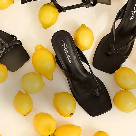 Elegante sorte sandaler blant gule sitroner.