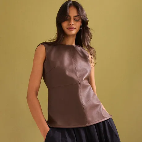 Elegant brun skinntopp uten ermer, kombinert med et mørkt skjørt og diskrete øredobber.